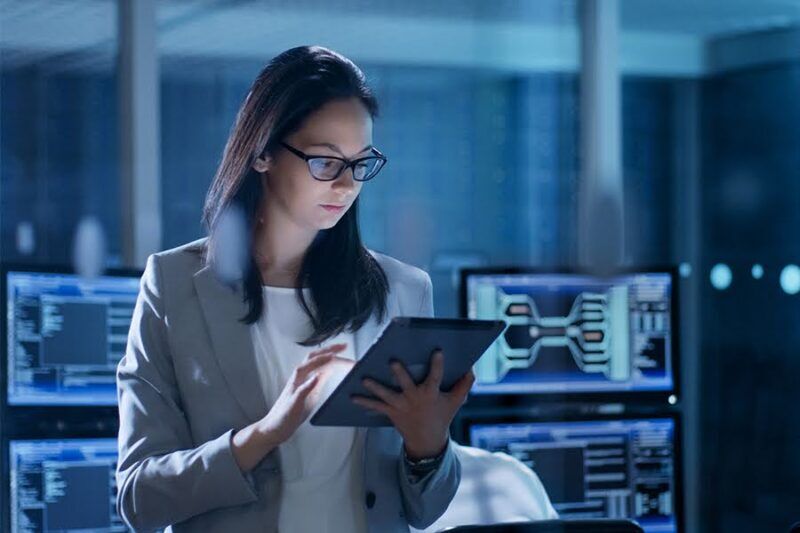 A woman in a business suit examines a tablet in a high-tech office, representing IT security in Hong Kong provided by EIRE Systems