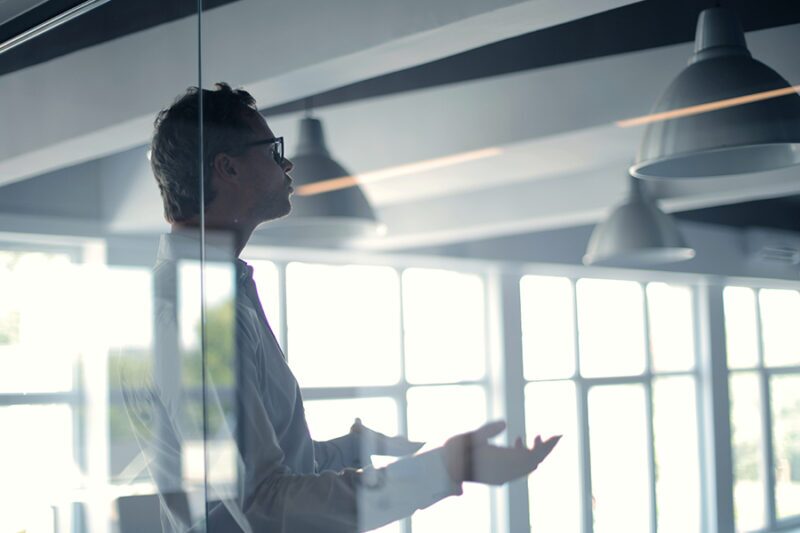 Close-up of IT project manager speaking during a meeting, observed through glass window Close-up of IT project manager speaking during a meeting, observed through glass