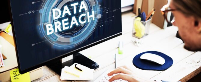 A person working at a computer displaying a prominent, glowing blue "DATA BREACH" graphic on the monitor.