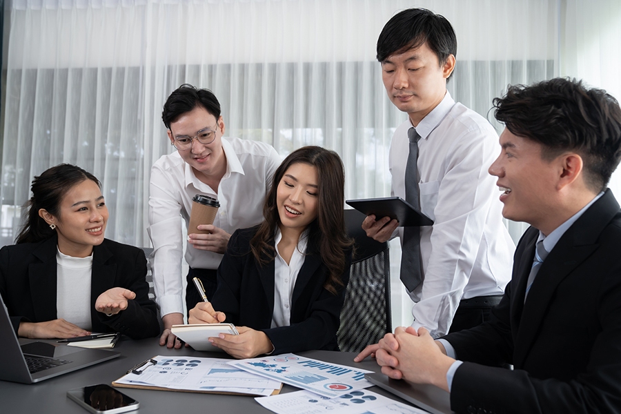 A team of professionals collaborating in an office, discussing charts and graphs, representing an IT services provider in Japan A team of professionals collaborating in an office, discussing charts and graphs, representing an IT services provider in Japan