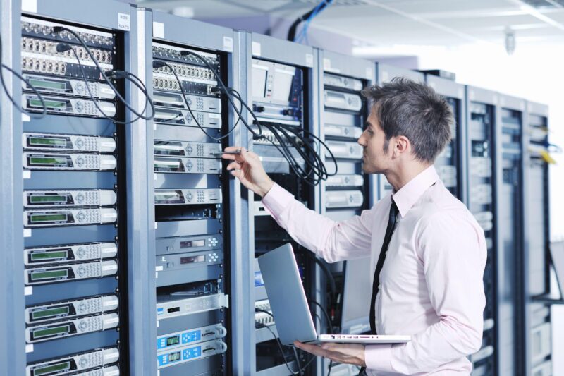 A man in a white shirt is inspecting data servers and network security.