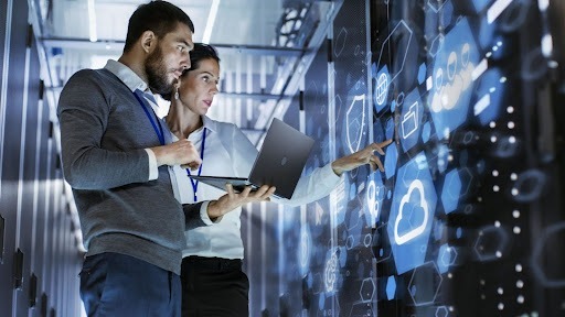 Two people working on a laptop surrounded by a cybersecurity network graphic, illustrating a vulnerability management concept.