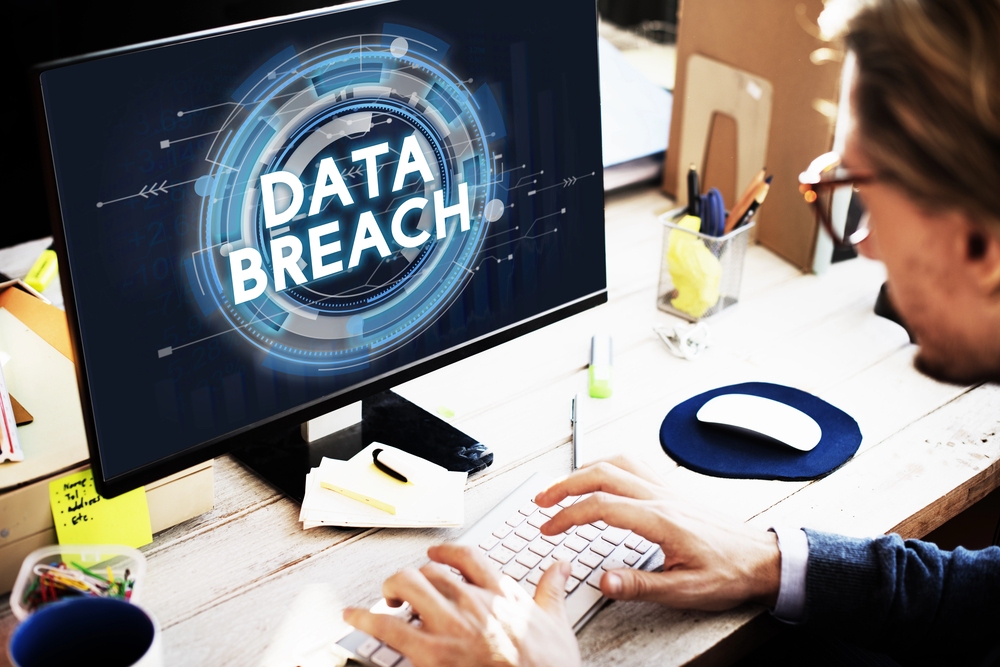 A person working at a computer displaying a prominent, glowing blue "DATA BREACH" graphic on the monitor.