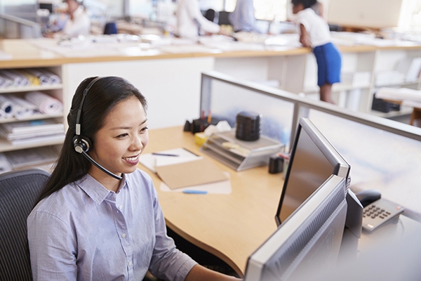 A professional woman providing IT Support in Tokyo, Japan, wearing a headset and working at her desk in a modern office environment