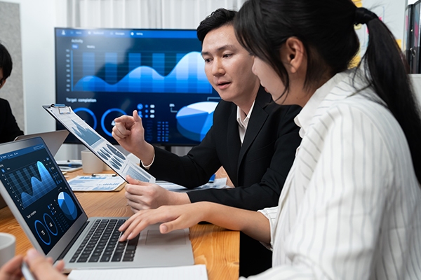 Business professionals discussing Japan IT Project Management, analyzing data charts on a laptop and presentation screen in an office