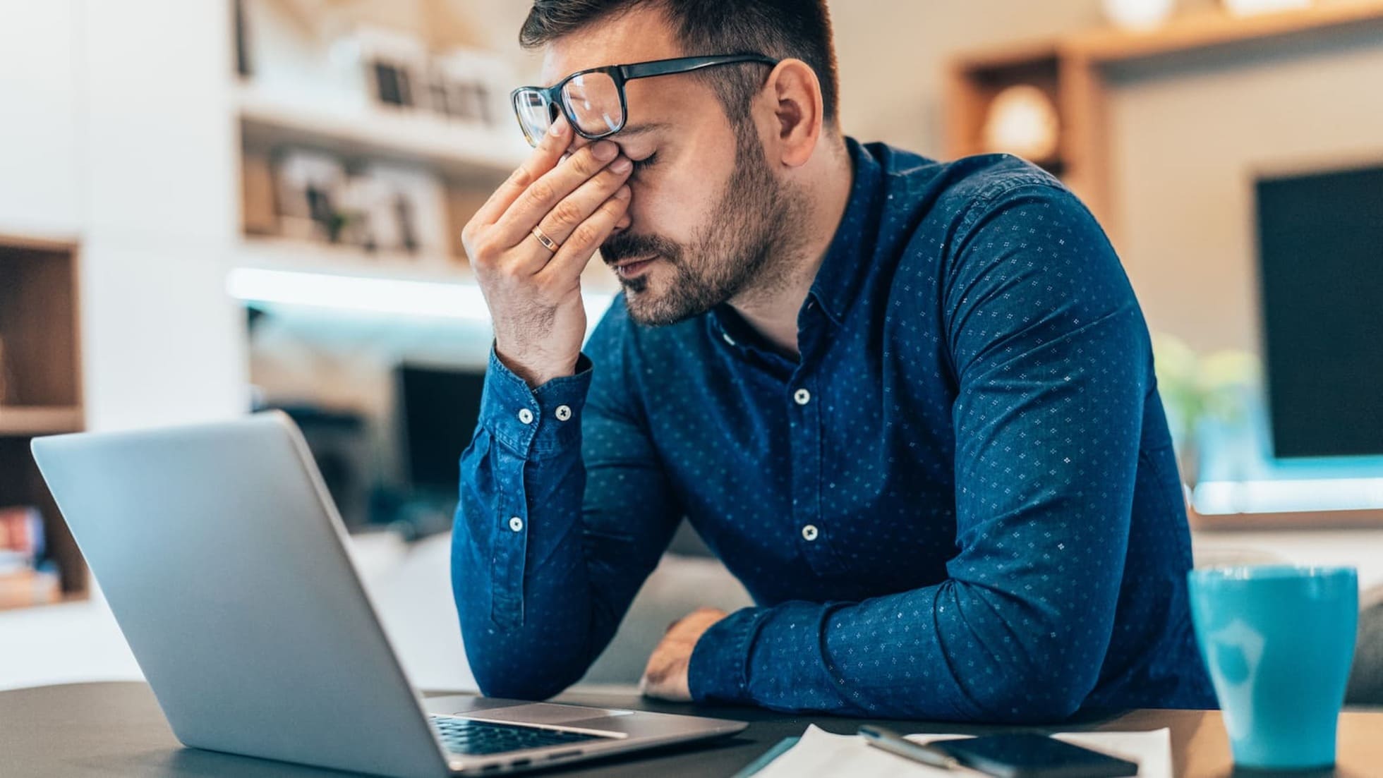 Frustrated young man in front of his laptop. Work gets disrupted due to connectivity issues caused by Wi-Fi.