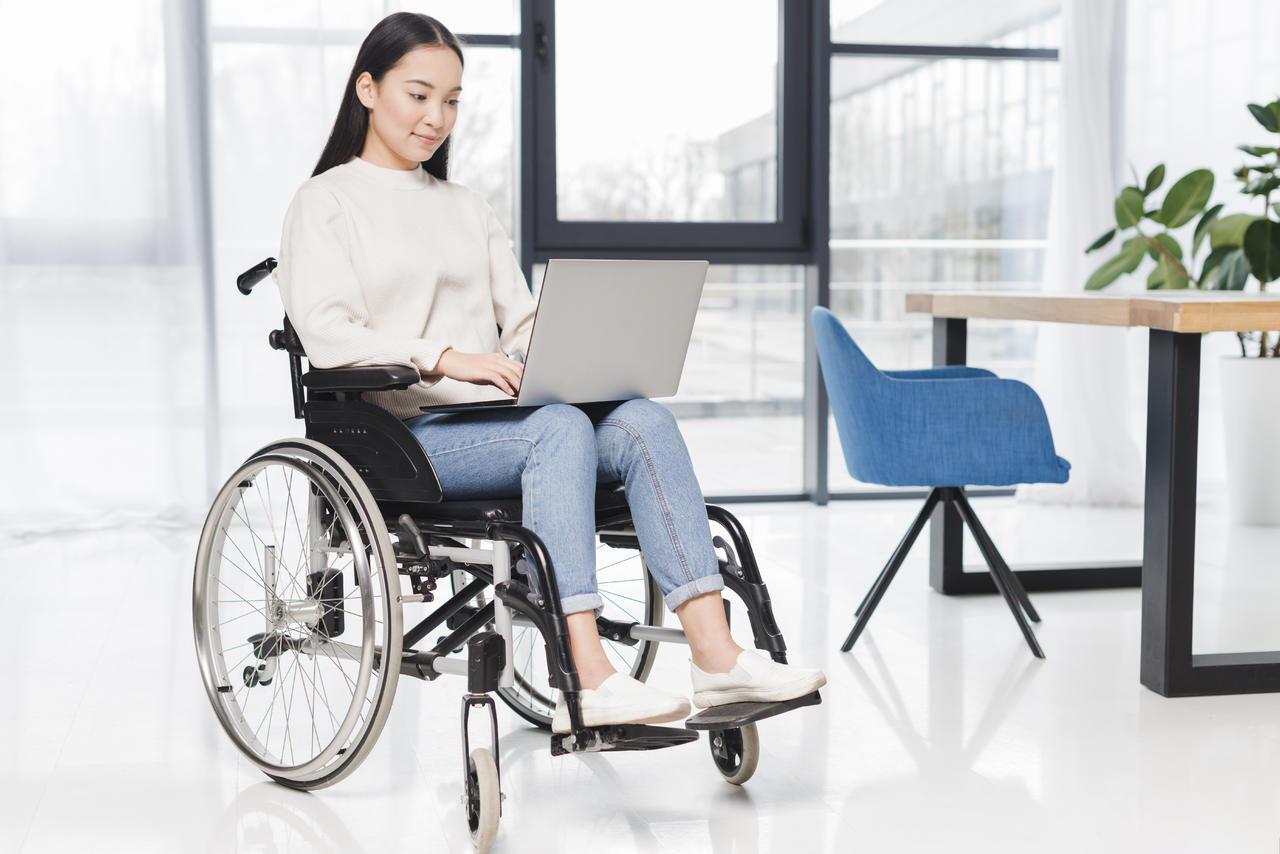 Young lady on a wheelchair using her laptop. She has accessible information technology for her disability.