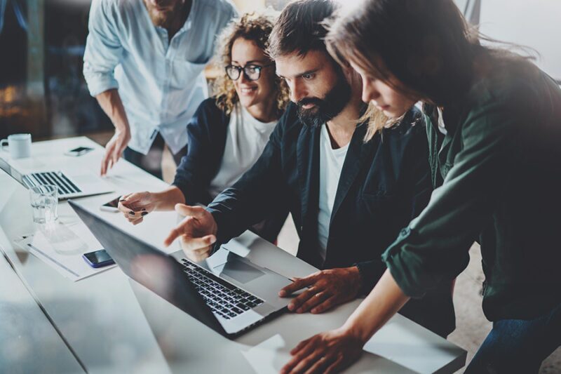 Group of professionals collaborating around a laptop, discussing industry-specific IT support solutions in an office