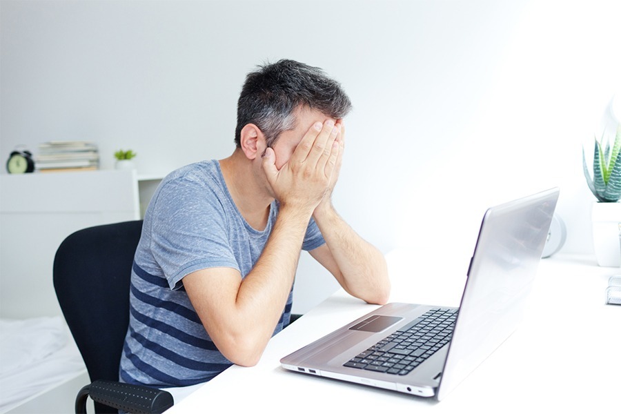 Man's hand on his face due to his laptop restarted unexpectedly which is one of the most common computer problems.