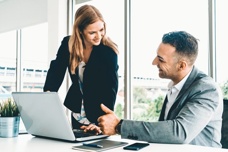 Two professionals discussing customized IT services while working on a laptop in a modern office setting.